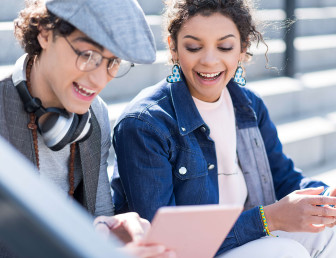 eye level view of two people sitting outside with man holding tablet device while woman holds mobile phone