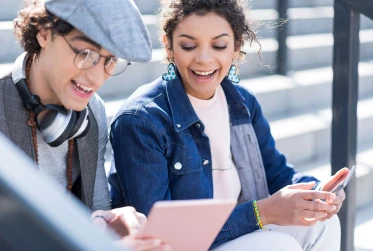 eye level view of two people sitting outside with man holding tablet device while woman holds mobile phone
