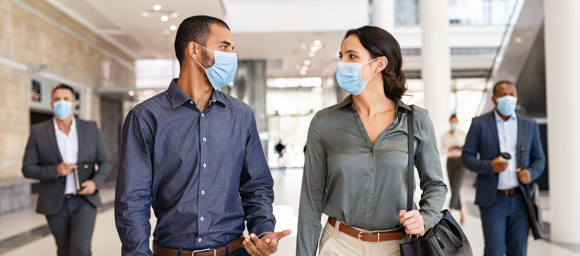 two people walking and talking with masks on with two people in background with masks on