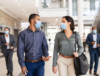 two people walking and talking with masks on with two people in background with masks on