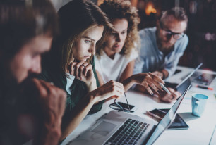 side view of four people at desk looking at a laptop