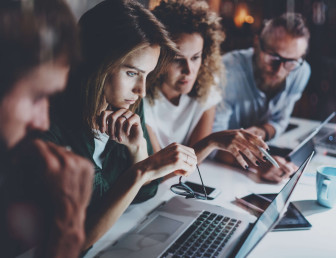 side view of four people at desk looking at a laptop