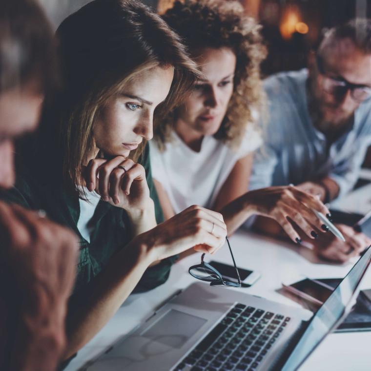 side view of four people at desk looking at a laptop