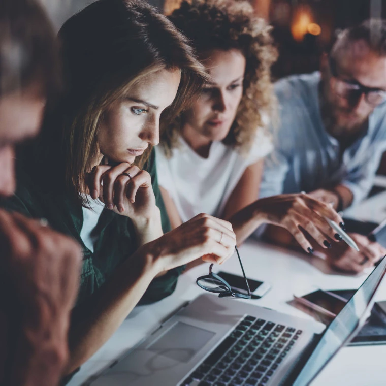 side view of four people at desk looking at a laptop