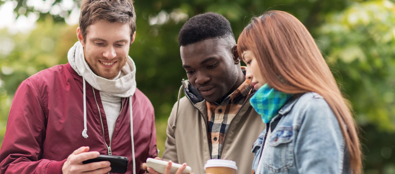 three people outside in casual clothing with one man holding phone while two others hold another phone