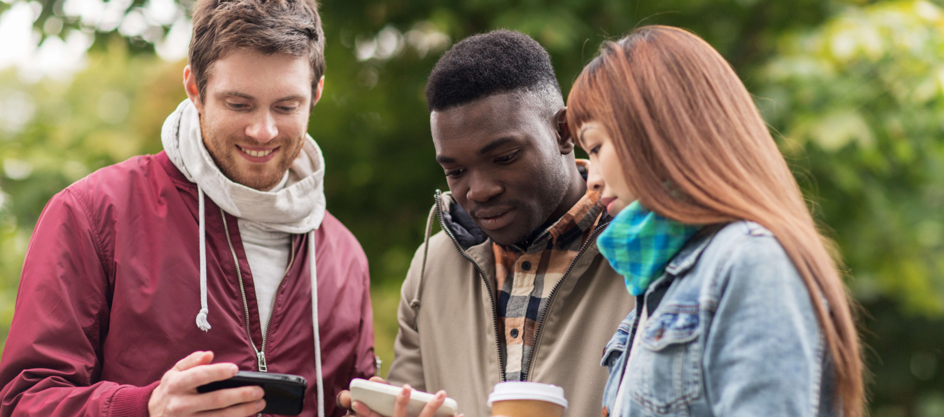 three people outside in casual clothing with one man holding phone while two others hold another phone