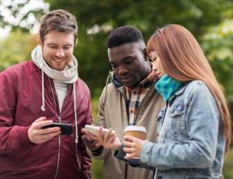 three people outside in casual clothing with one man holding phone while two others hold another phone