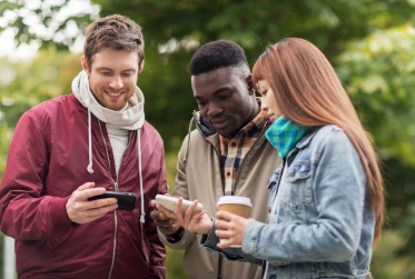 three people outside in casual clothing with one man holding phone while two others hold another phone