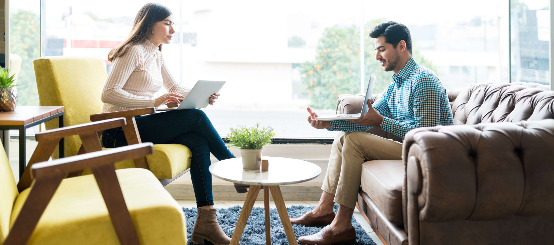 side view of two people in a lobby setting with both holding laptops