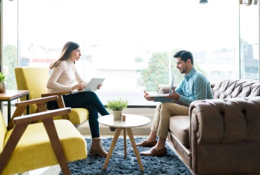 side view of two people in a lobby setting with both holding laptops