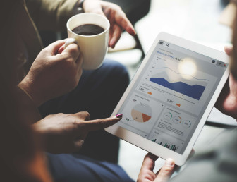birds eye view of man holding tablet device with data on the screen with two others interacting