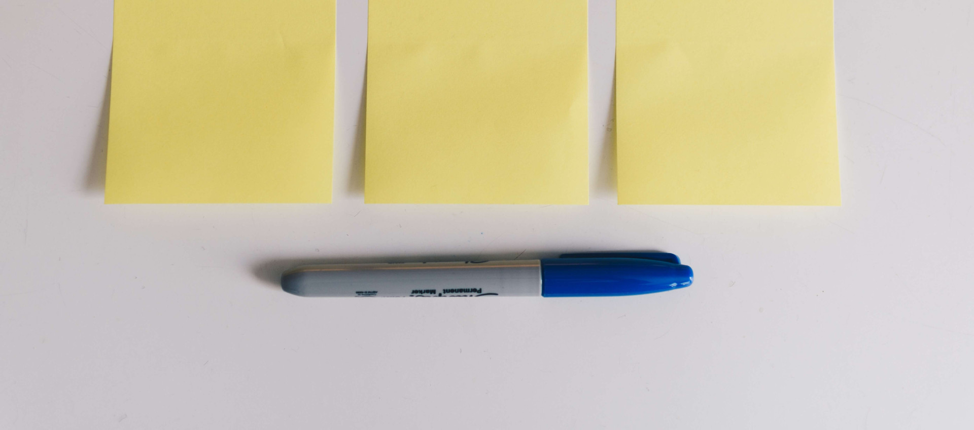 three yellow post it notes with blue sharpy pen underneath on white surface
