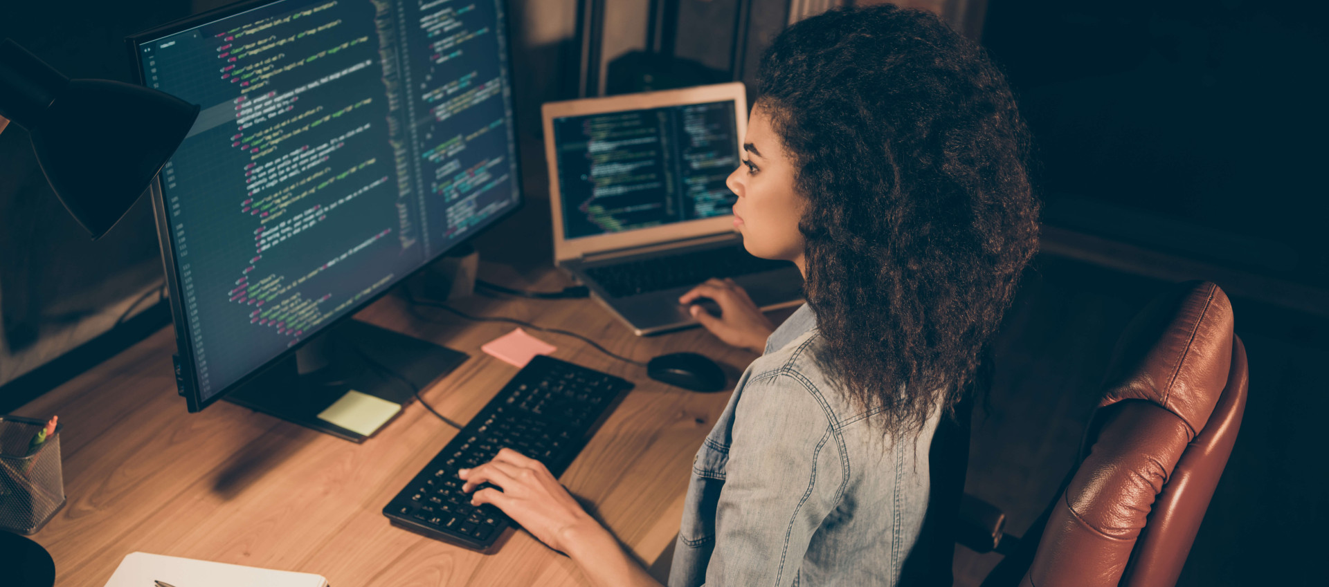 birds eye view of woman working on coding with one hand on laptop keyboard and the other on desktop keyboard