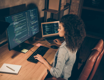 birds eye view of woman working on coding with one hand on laptop keyboard and the other on desktop keyboard