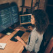 birds eye view of woman working on coding with one hand on laptop keyboard and the other on desktop keyboard