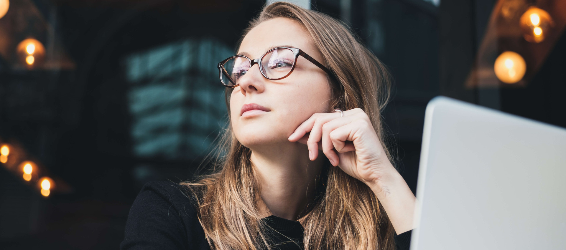 low angle view of woman wearing glasses looking to her right with laptop in front of her