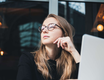 low angle view of woman wearing glasses looking to her right with laptop in front of her