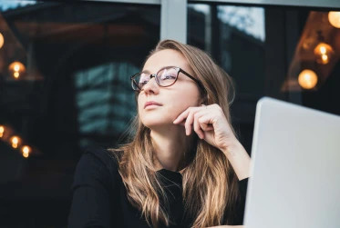 low angle view of woman wearing glasses looking to her right with laptop in front of her