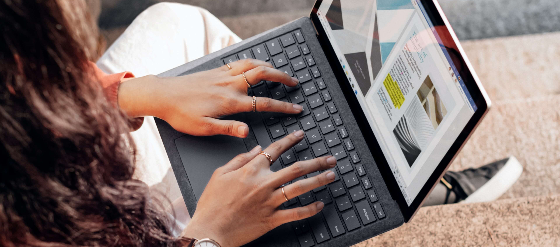 birds eye view of woman sitting outside working on laptop with drink and papers beside her