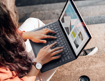 birds eye view of woman sitting outside working on laptop with drink and papers beside her