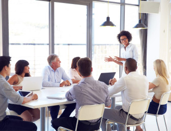 woman leading meeting with seven other people sitting at a table