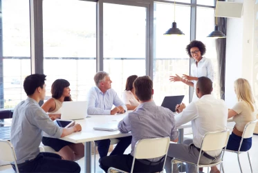woman leading meeting with seven other people sitting at a table