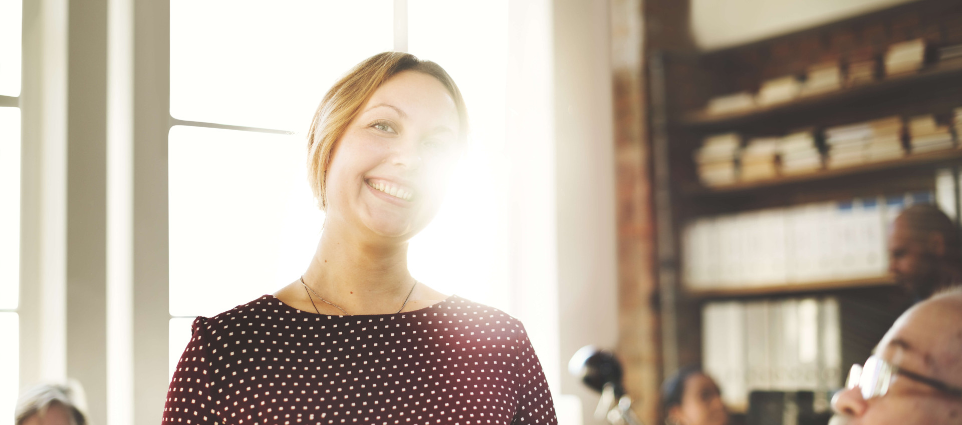 eye level view of woman in an office smiling directly at camera with people in the background