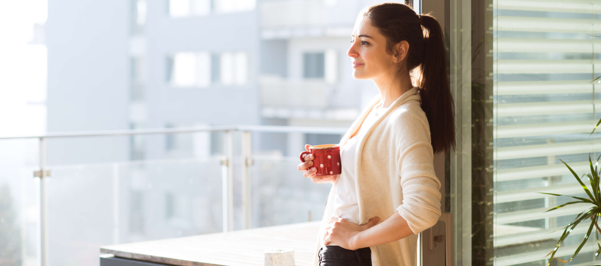 woman smiling holding cup of coffee looking out from the balcony