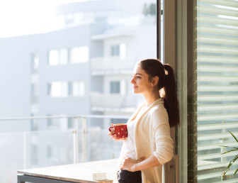 woman smiling holding cup of coffee looking out from the balcony