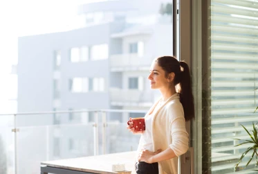 woman smiling holding cup of coffee looking out from the balcony