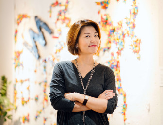 eye level view of woman grinning with arms folded looking at the camera with multicoloured background 