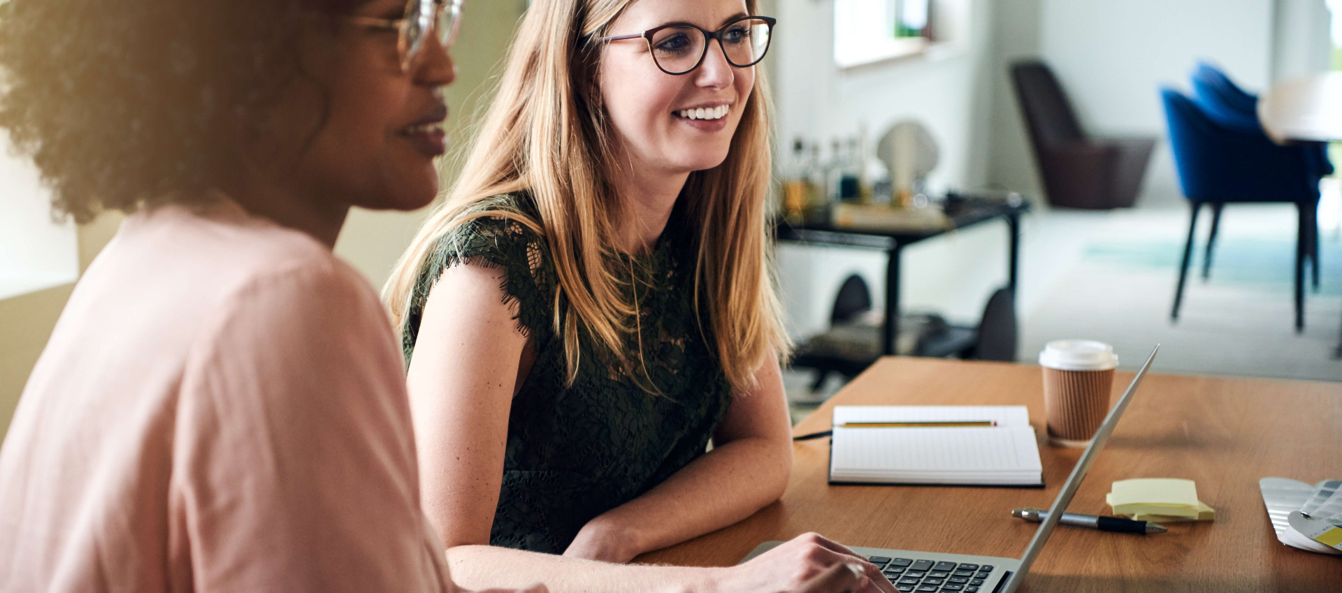 eye level view of two women at a table with laptop in front speaking to others out of view