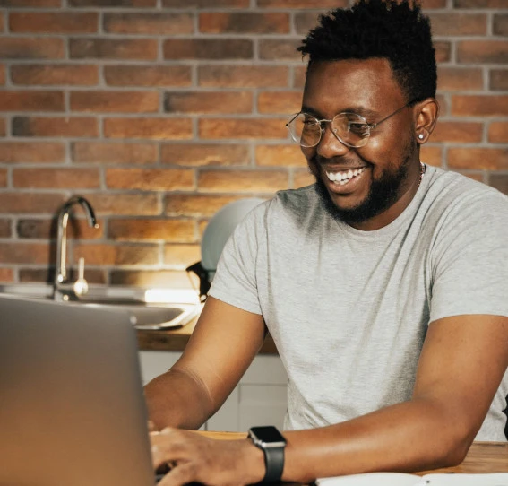 A man  wearing glasses, gazes at his laptop screen with. He is at his home's kitchen table.