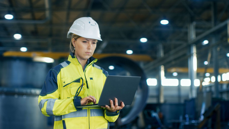 female industrial worker with a laptop in hand wearing protective clothing and helmet