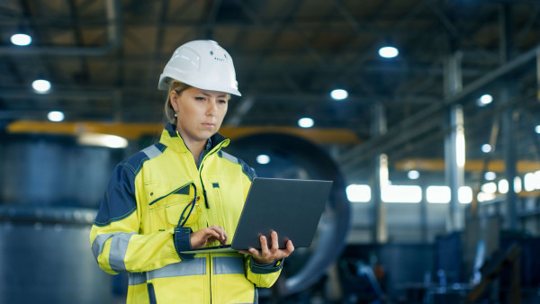 female industrial worker with a laptop in hand wearing protective clothing and helmet