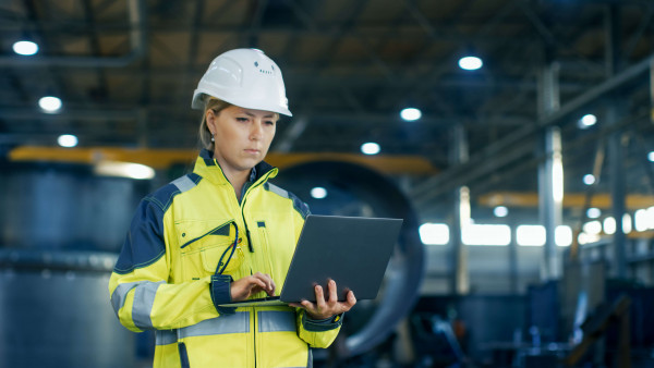 female industrial worker with a laptop in hand wearing protective clothing and helmet