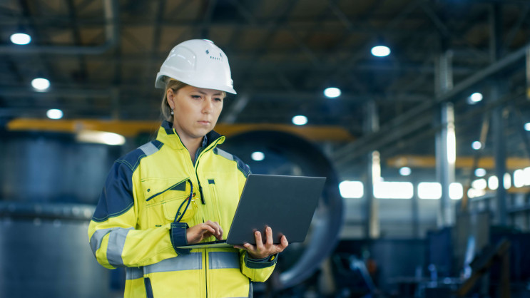 female industrial worker with a laptop in hand wearing protective clothing and helmet