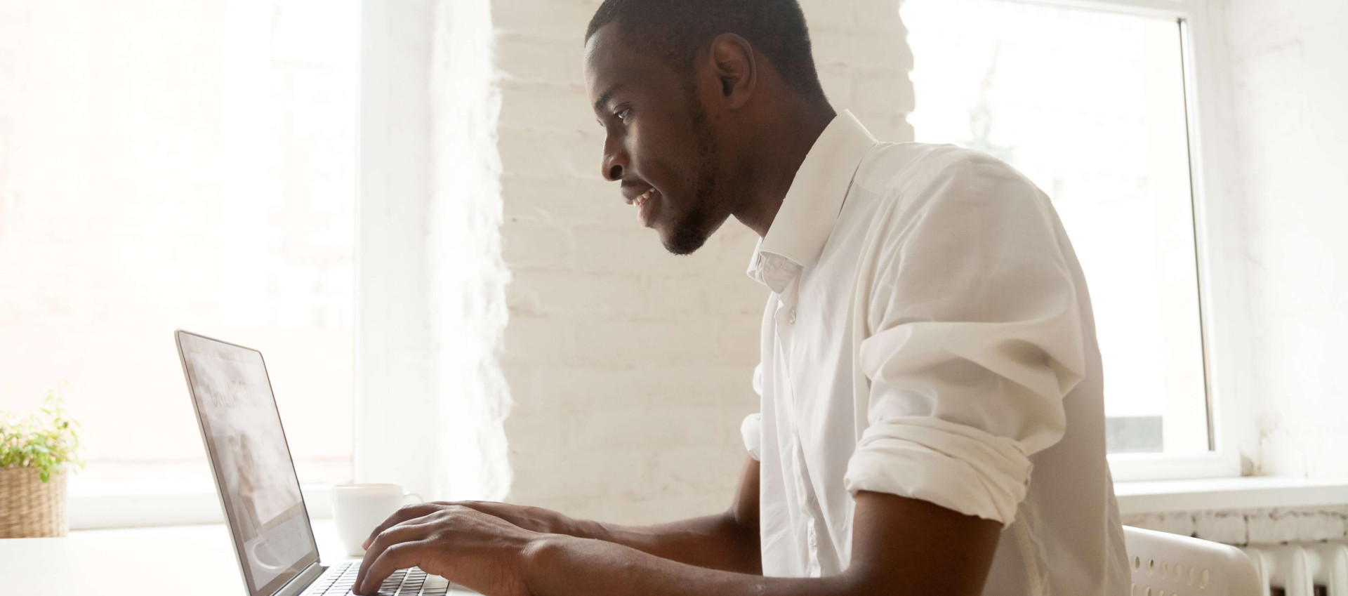 side view of man dressed in white working on a laptop in white office