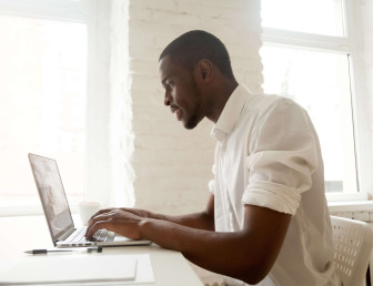 side view of man dressed in white working on a laptop in white office