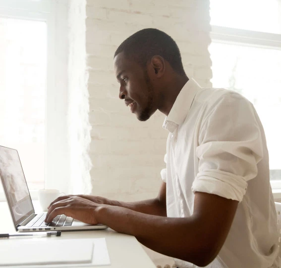 side view of man dressed in white working on a laptop in white office