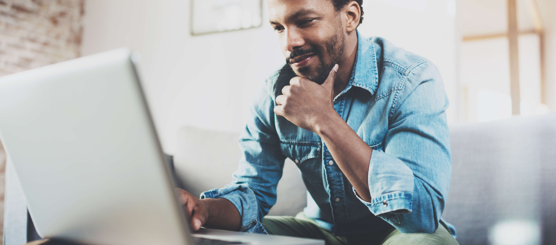 man wearing casual clothes sitting on sofa looking at laptop