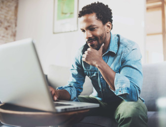 man wearing casual clothes sitting on sofa looking at laptop