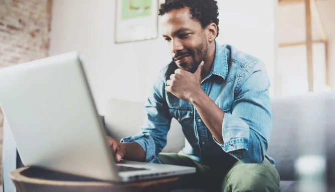 man wearing casual clothes sitting on sofa looking at laptop