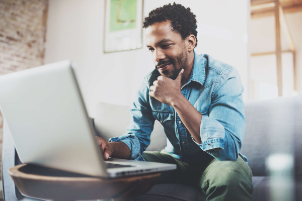 man wearing casual clothes sitting on sofa looking at laptop