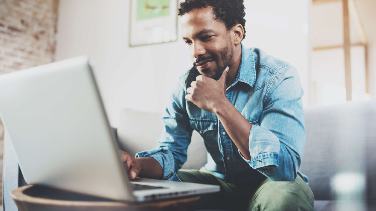 man wearing casual clothes sitting on sofa looking at laptop