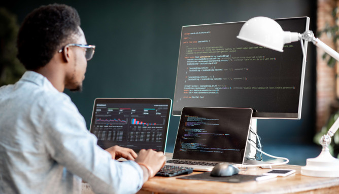man working on coding using desktop screen and two laptops on a desk