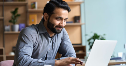 eye level view of bearded man in smart clothes smiling at laptop in an office