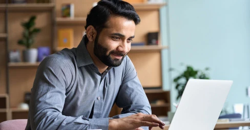 eye level view of bearded man in smart clothes smiling at laptop in an office