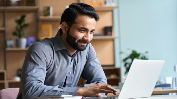 eye level view of bearded man in smart clothes smiling at laptop in an office