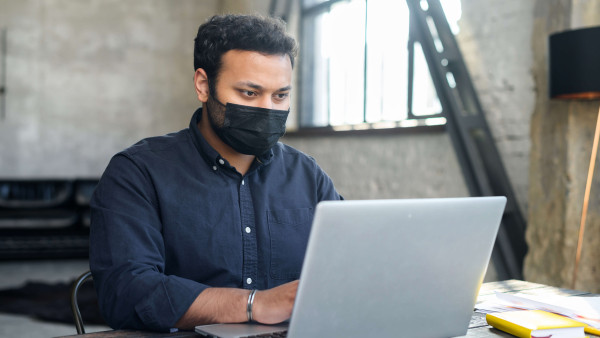 man in an office on a laptop while holding mobile phone